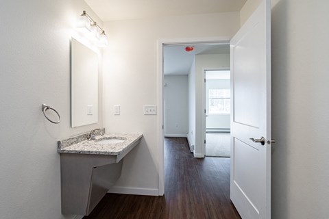 a bathroom with a sink and mirror and a hallway with a door to a bedroom