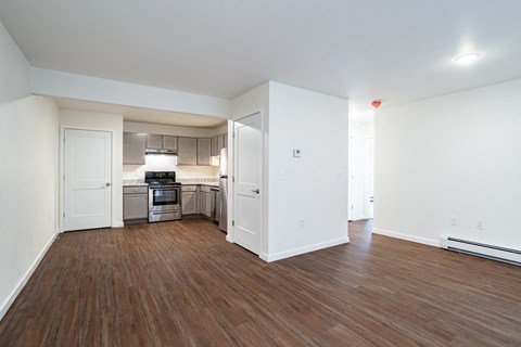 an empty living room and kitchen with wood flooring and white walls