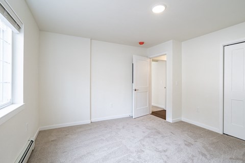 a bedroom with white walls and carpet and a door to a closet