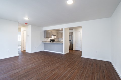 the living room and kitchen of an apartment with white walls and wood flooring