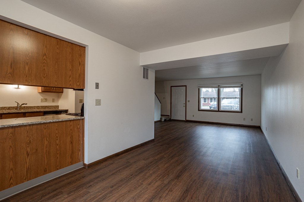 an empty living room and kitchen with wood floors and white walls