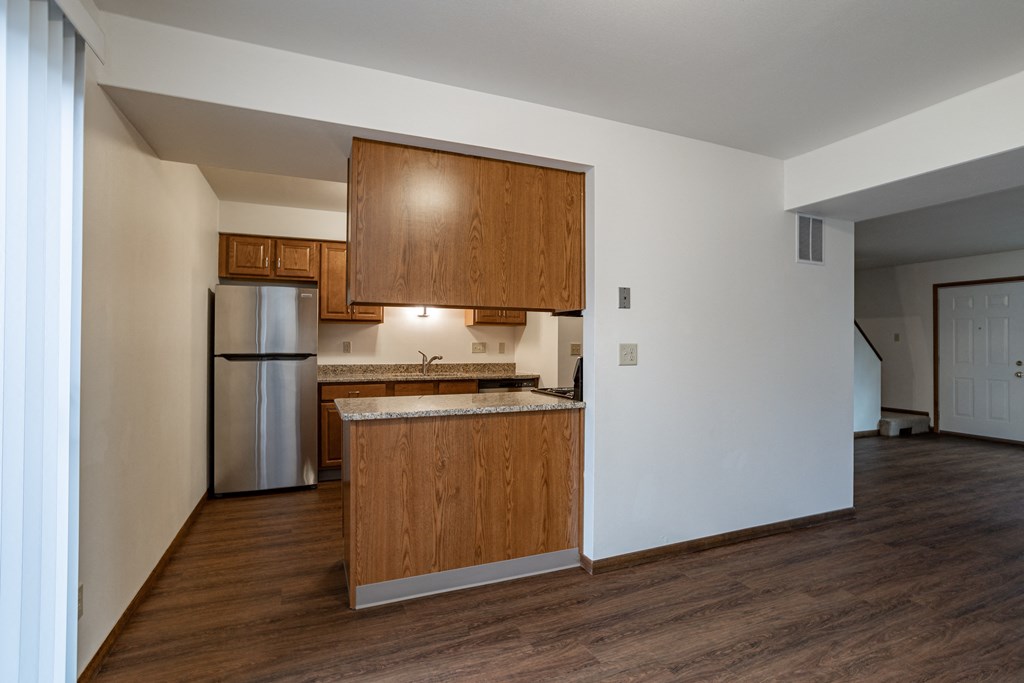 an empty kitchen with wooden cabinets and a stainless steel refrigerator
