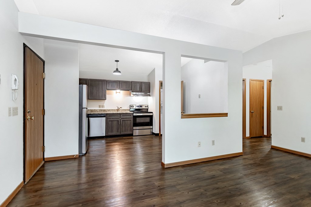 an empty living room and kitchen with wood floors and white walls