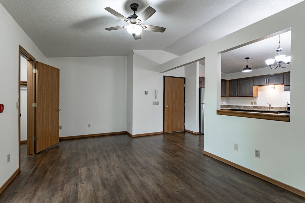 an empty living room with a ceiling fan and a kitchen