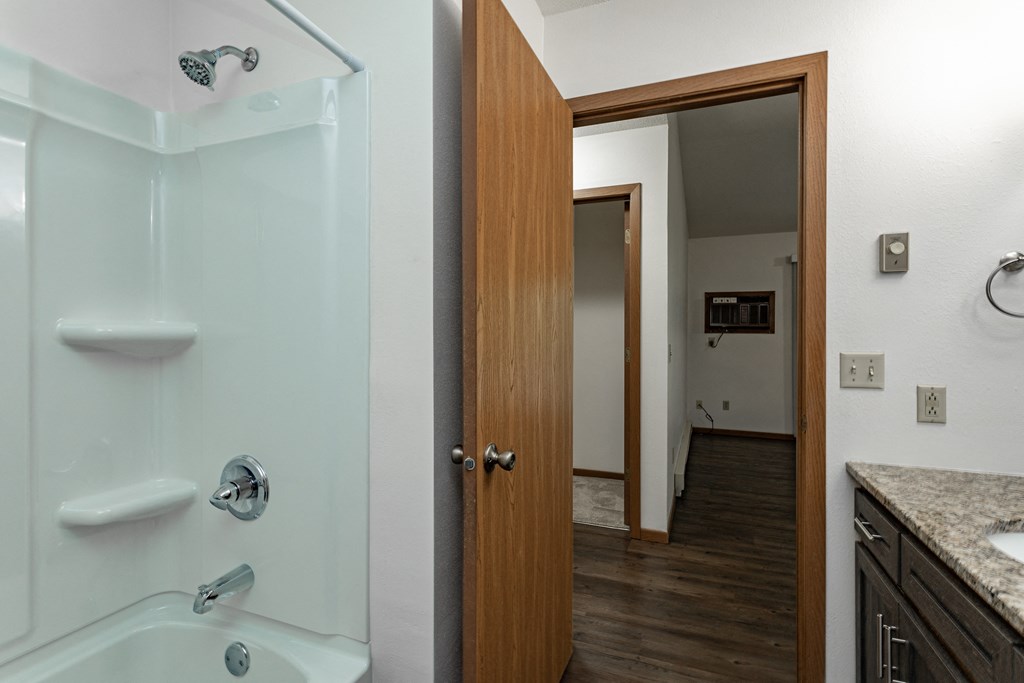 a bathroom with a shower and a sink and a door to a hallway