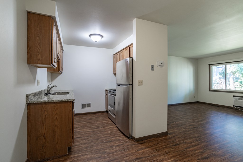 an empty living room with a refrigerator and a kitchen