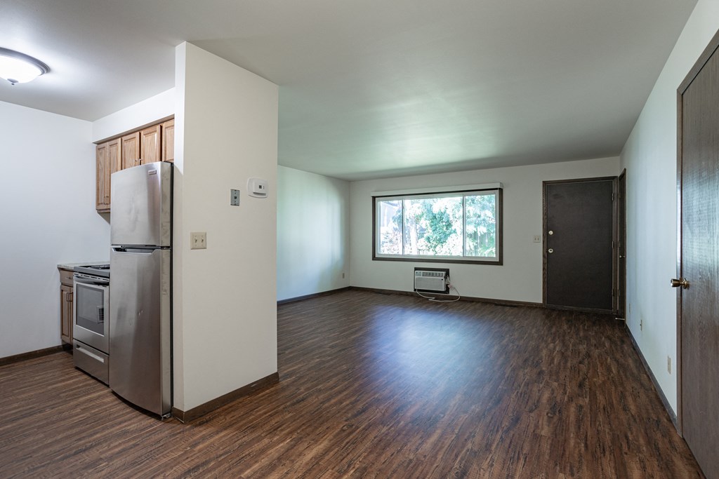 an empty living room with a refrigerator and a window