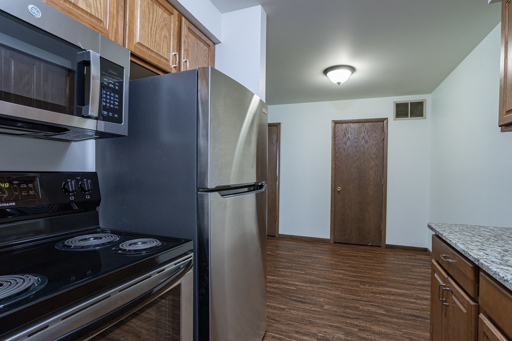a kitchen with stainless steel appliances and wood flooring and a door to a hallway