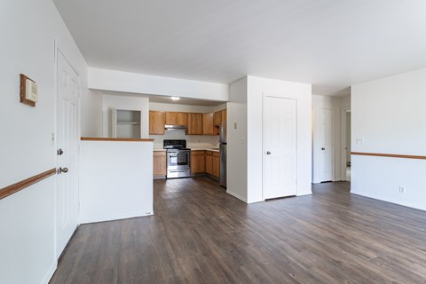 an empty living room and kitchen with wood floors and white walls
