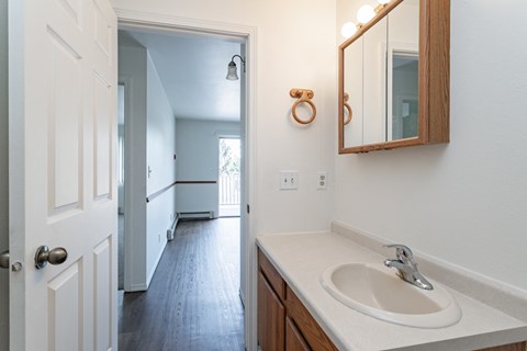 a bathroom with a sink and a mirror and a hallway to a bedroom