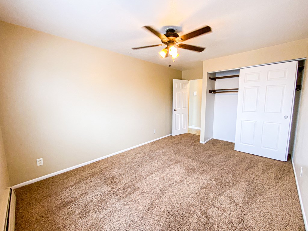 an empty living room with a ceiling fan and a closet