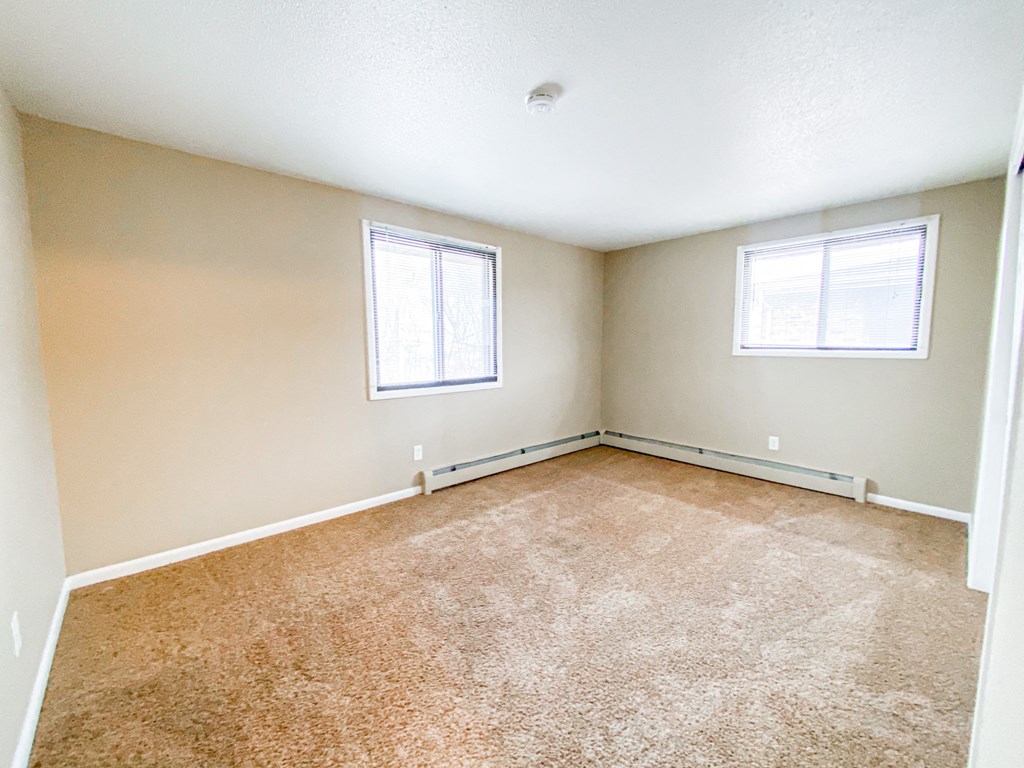 an empty living room with carpet and two windows