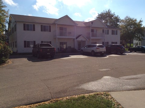 A white building with a pink roof and a parking lot in front.