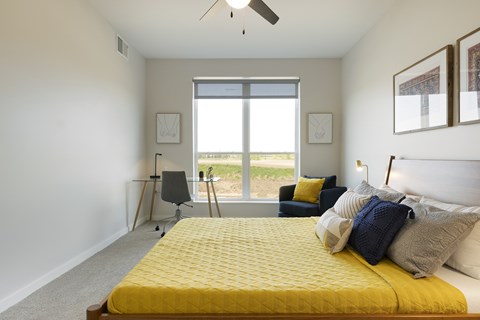 A bedroom with a yellow bed and a window overlooking the grass.