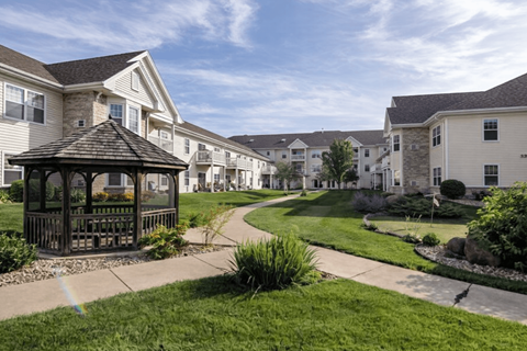 A gazebo sits in the middle of a grassy area in front of apartment buildings.