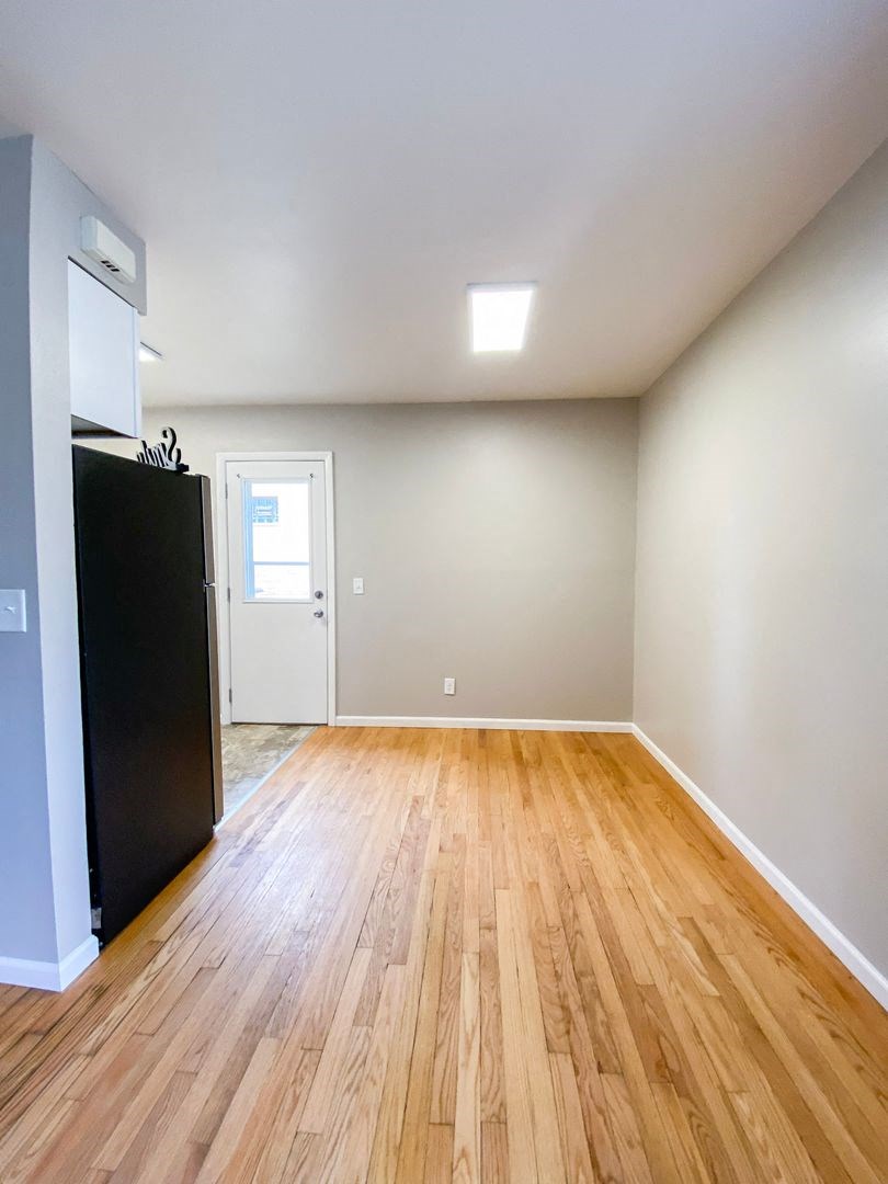 an empty living room with wood floors and a refrigerator