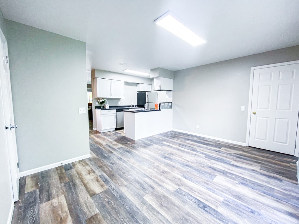 an empty living room and kitchen with wood flooring