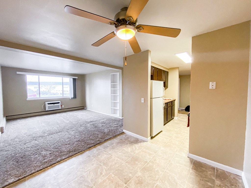 an empty living room with a ceiling fan and a kitchen