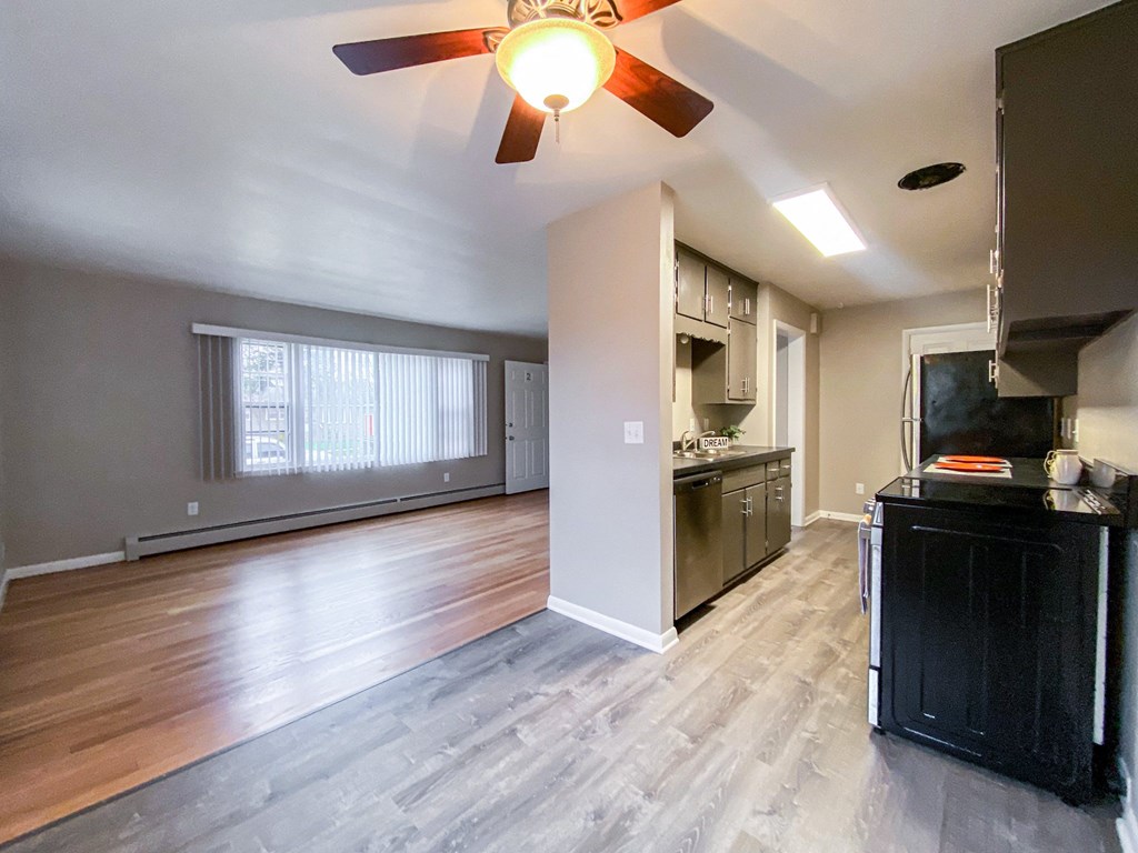 an empty living room with a kitchen and a ceiling fan
