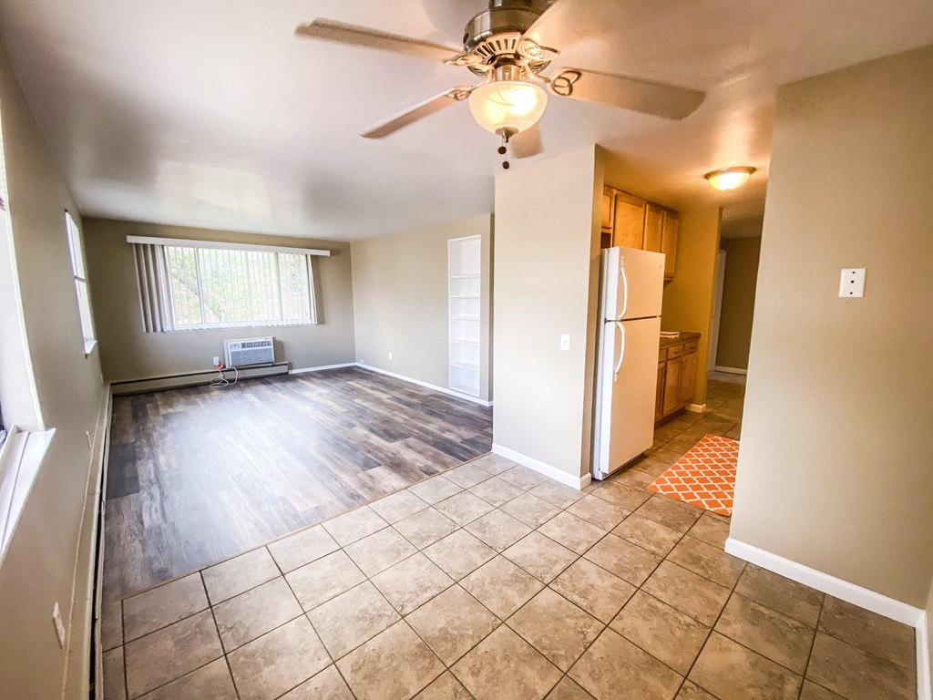 an empty living room with a kitchen and a ceiling fan