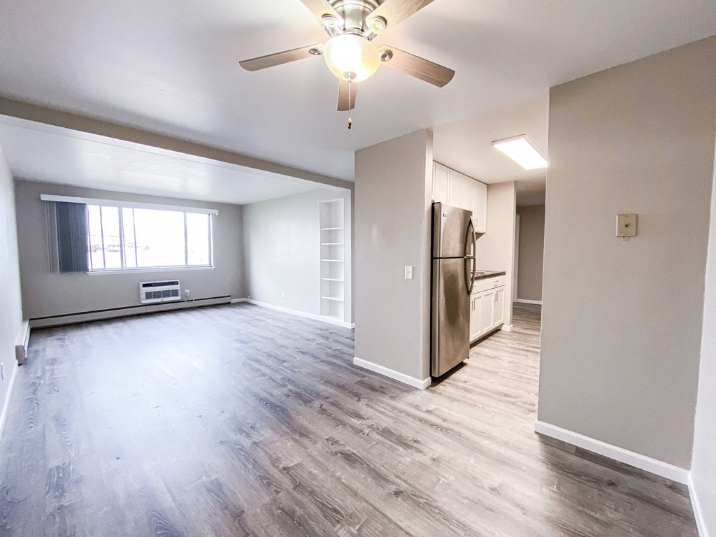 an empty living room with a ceiling fan and a refrigerator
