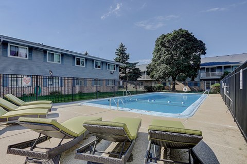 A pool surrounded by lounge chairs and apartment buildings.