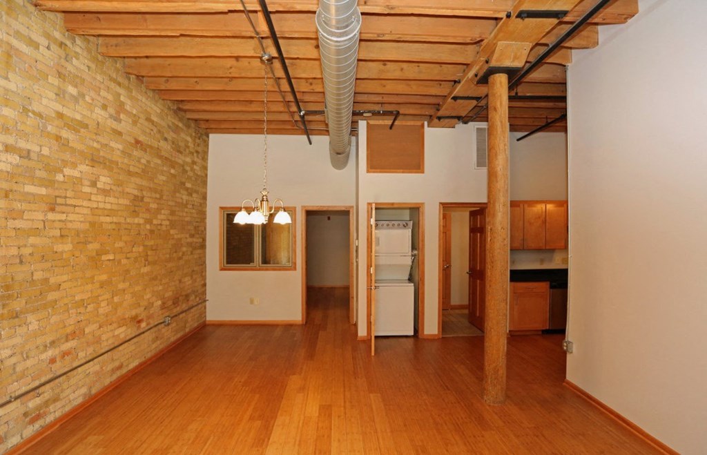 an empty living room with a brick wall and wood floors