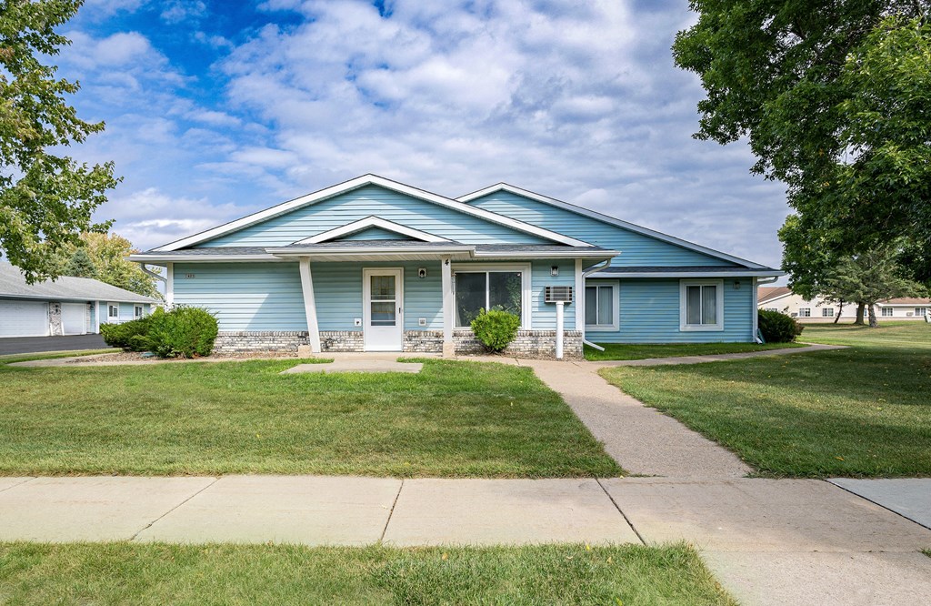 the front of a blue house with a sidewalk and grass