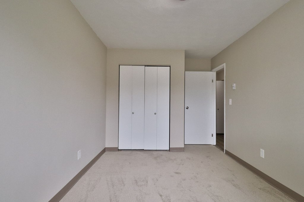 a living room with white walls and a carpet and two closets