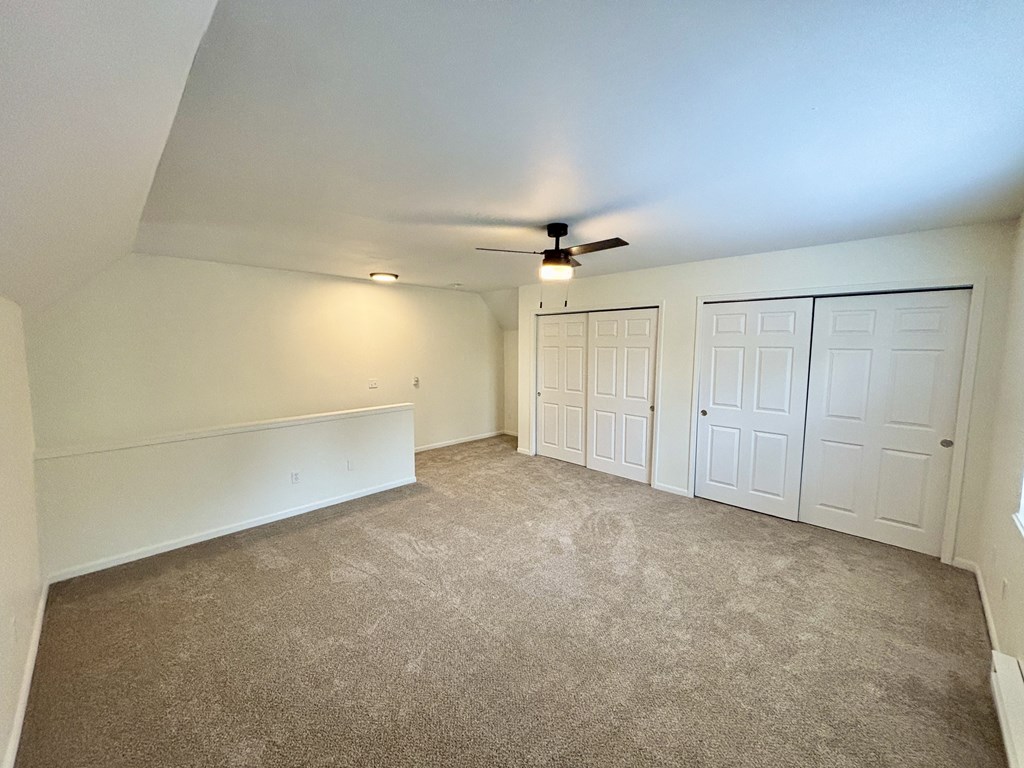 A room with a carpeted floor and a ceiling fan.