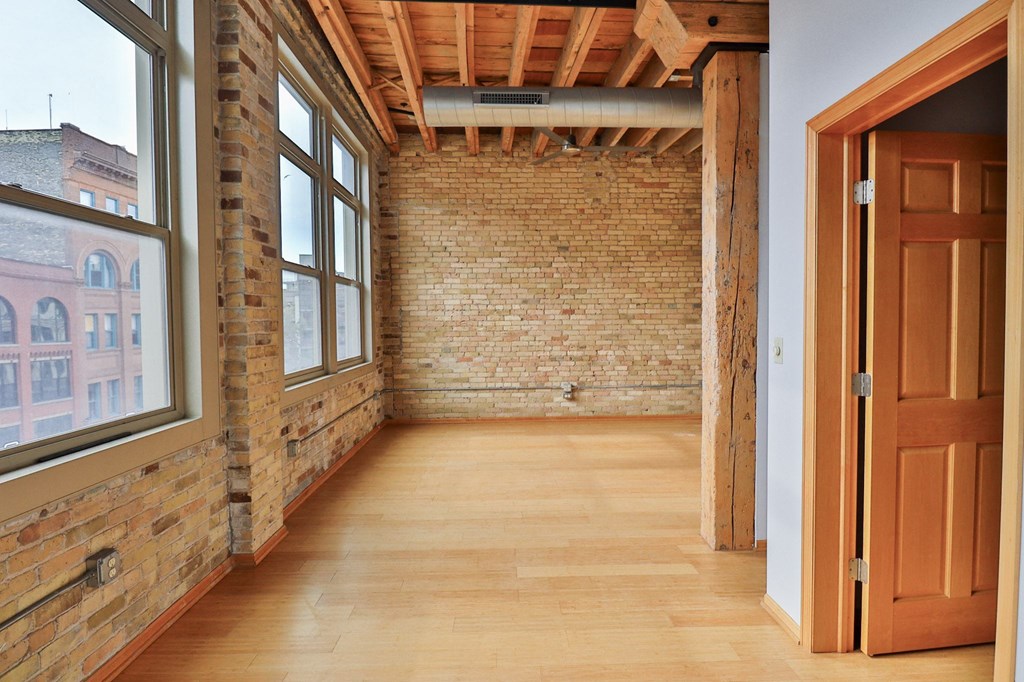 an empty room with brick wall and wooden floors and a wooden door