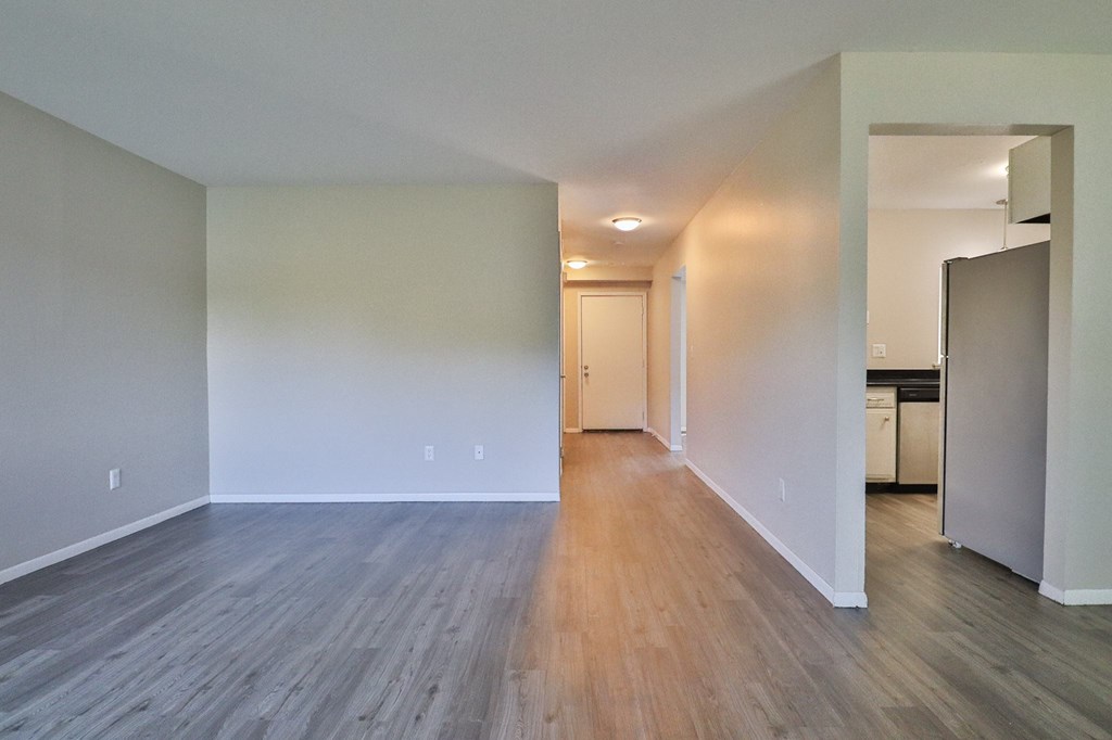 an empty living room with wood flooring and a kitchen