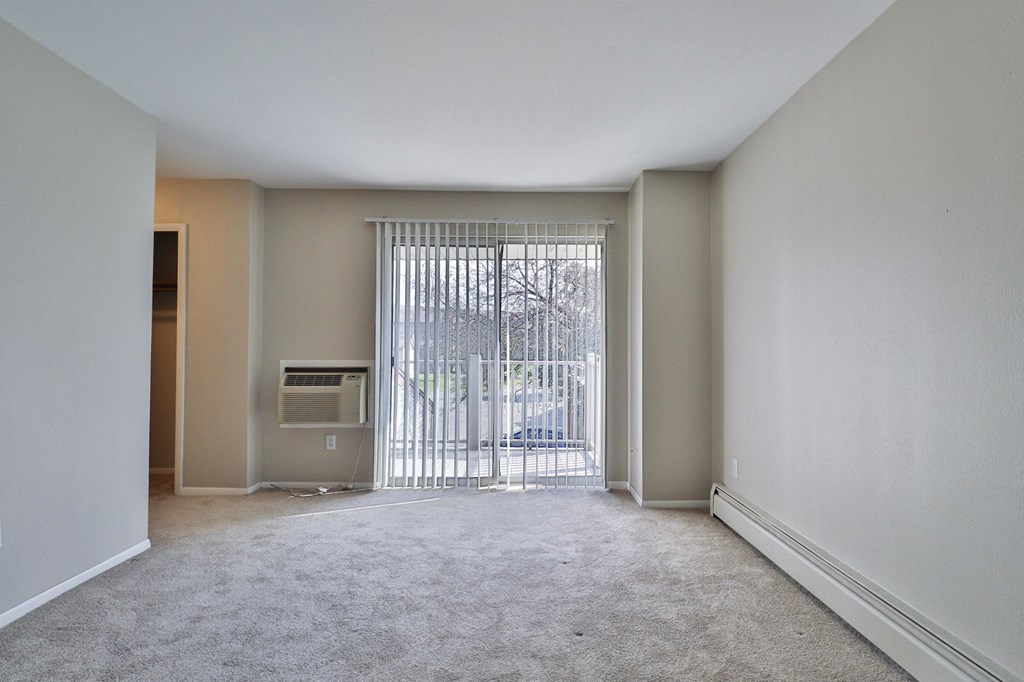 an empty living room with a sliding glass door to a balcony