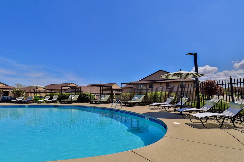 A swimming pool surrounded by lounge chairs and a fence.