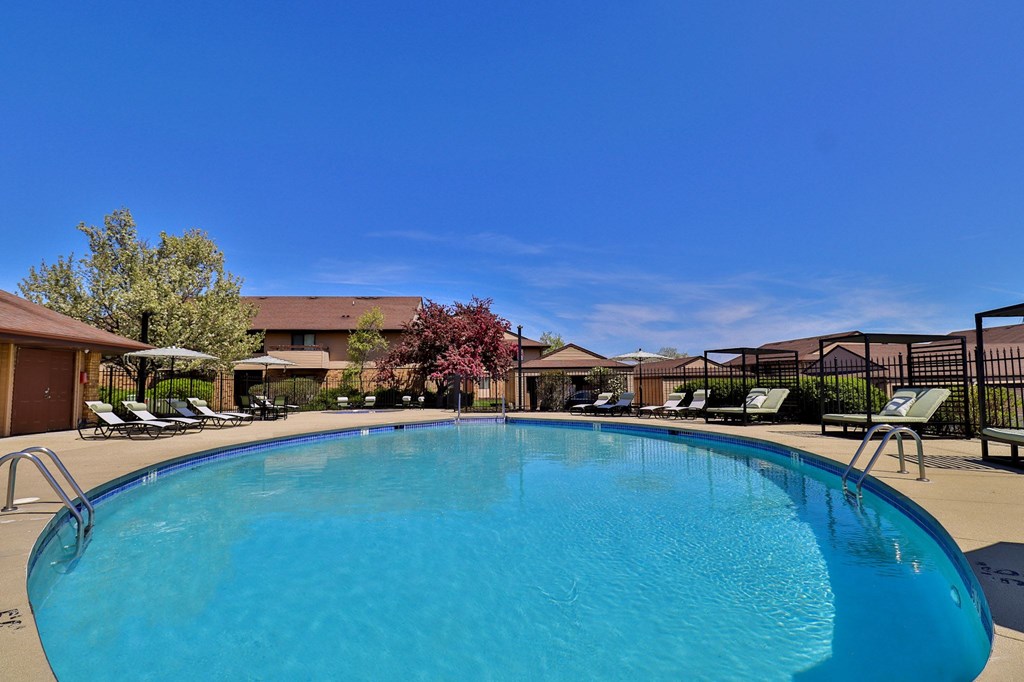 A large blue swimming pool in front of a building with a fence and trees.