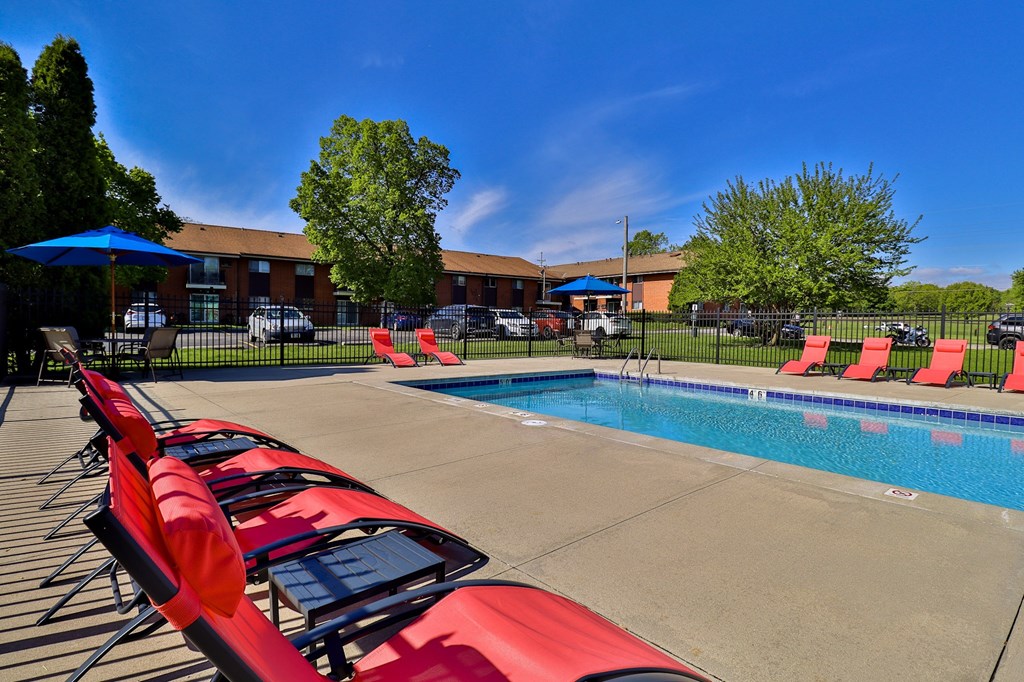 A poolside with red sun loungers and a blue umbrella.