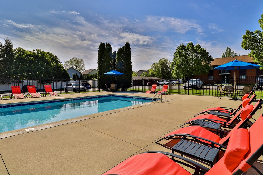 A pool surrounded by red chairs and a blue umbrella.