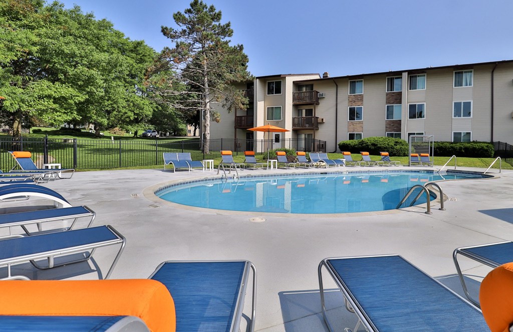 A swimming pool surrounded by sun loungers and apartment buildings.