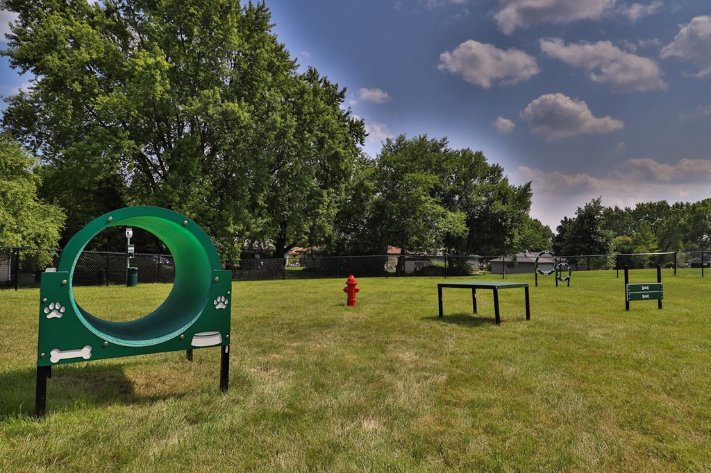 A dog park with a green tunnel and a red fire hydrant.
