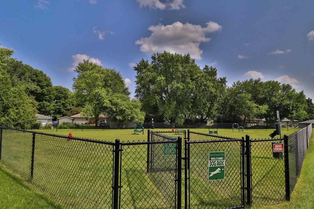 A black fence with a green sign that says Dog Park.