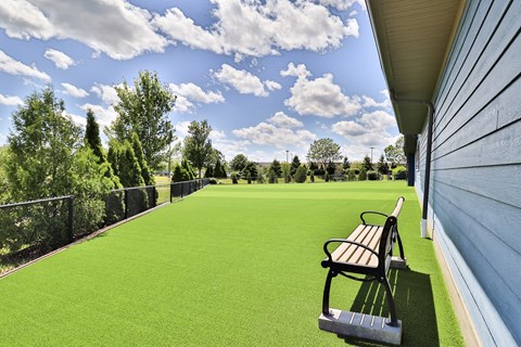 A bench sits on a green lawn next to a house.