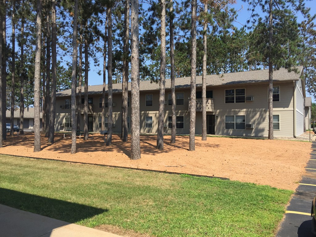 A building with a brown roof and tan walls is surrounded by tall pine trees.