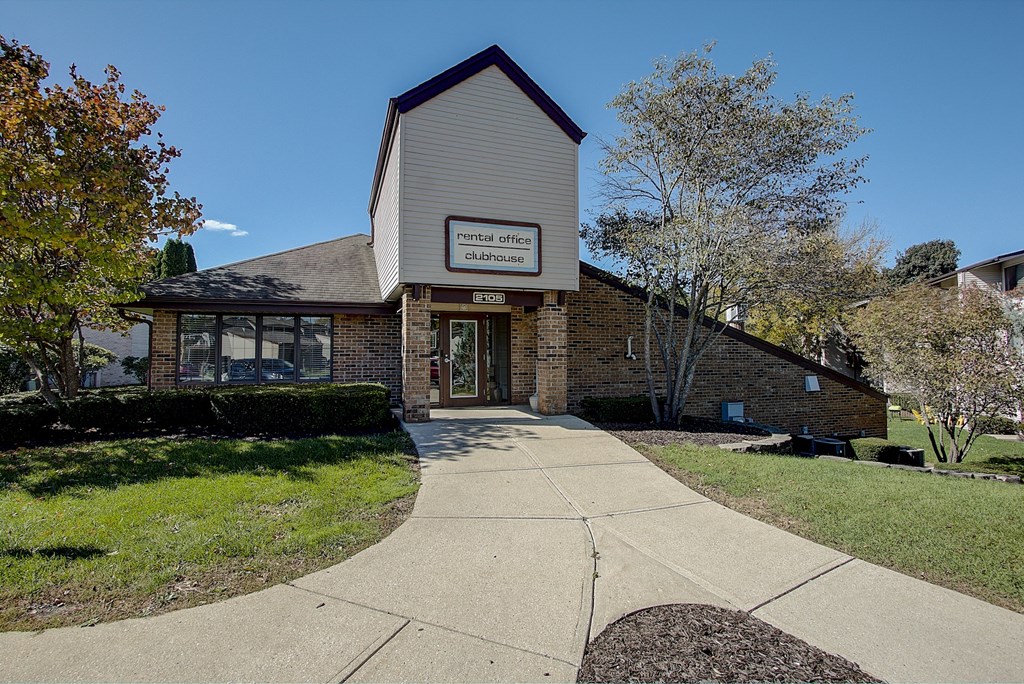 a walkway leads to the front door of a brick building with a sign on the front