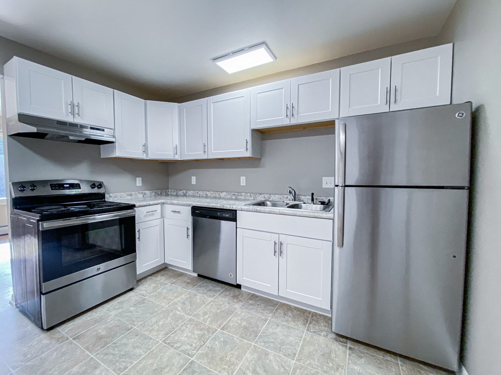 an empty kitchen with stainless steel appliances and white cabinets
