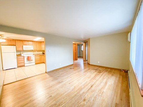 A room with wooden floors and a kitchen area to the left.