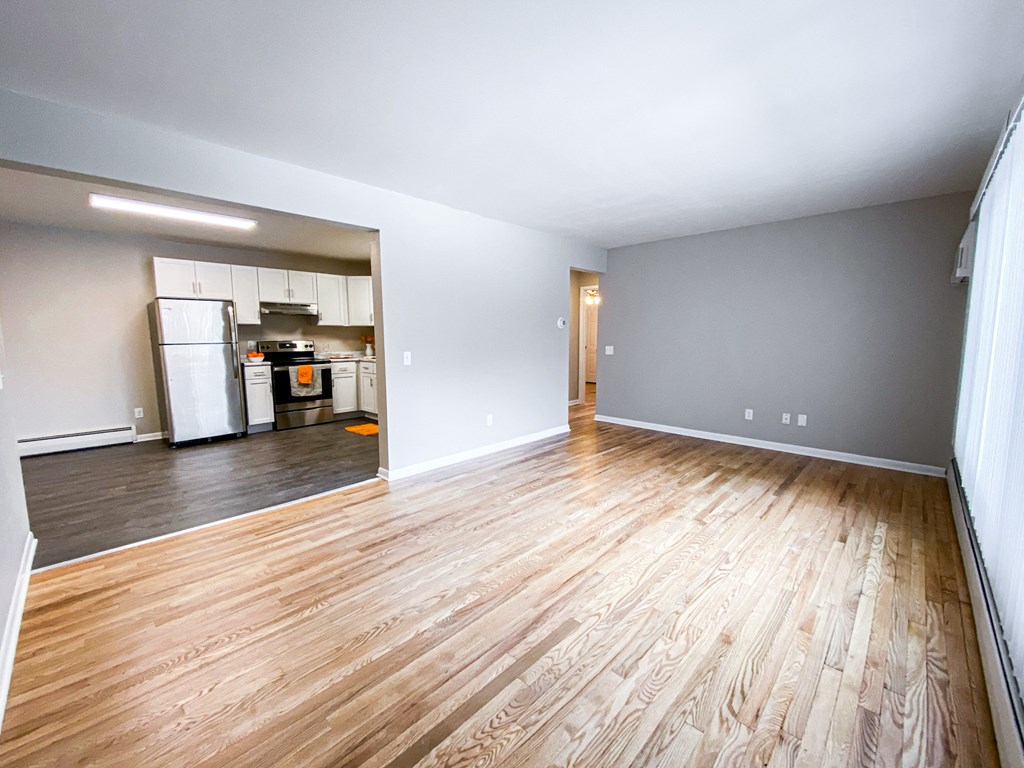 an empty living room with wood floors and a kitchen