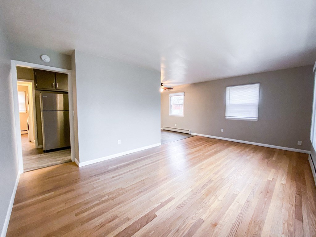 an empty living room with wood flooring and a kitchen