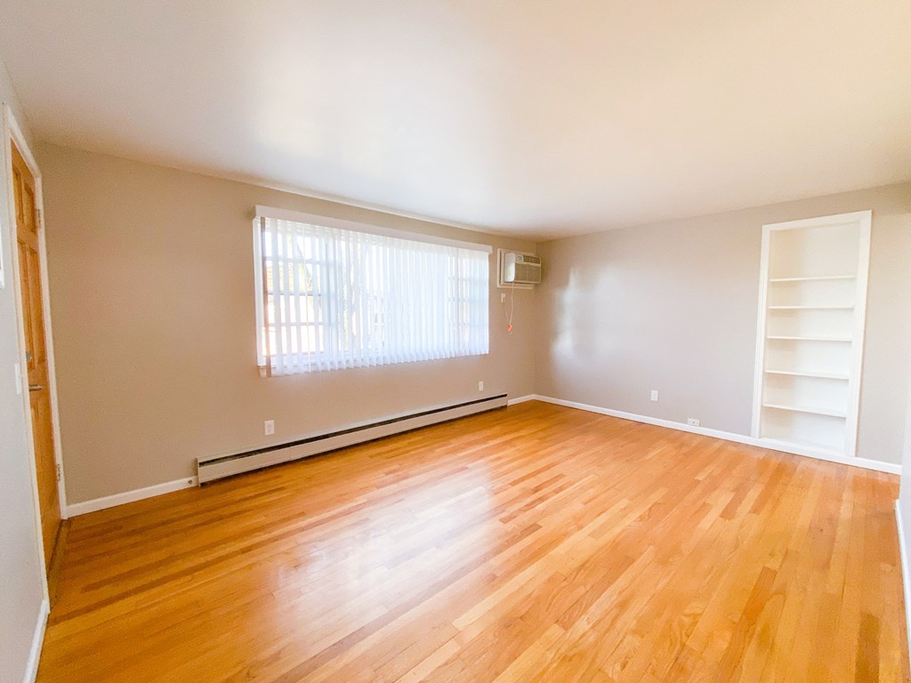 an empty living room with wooden floors and a window and white shelves