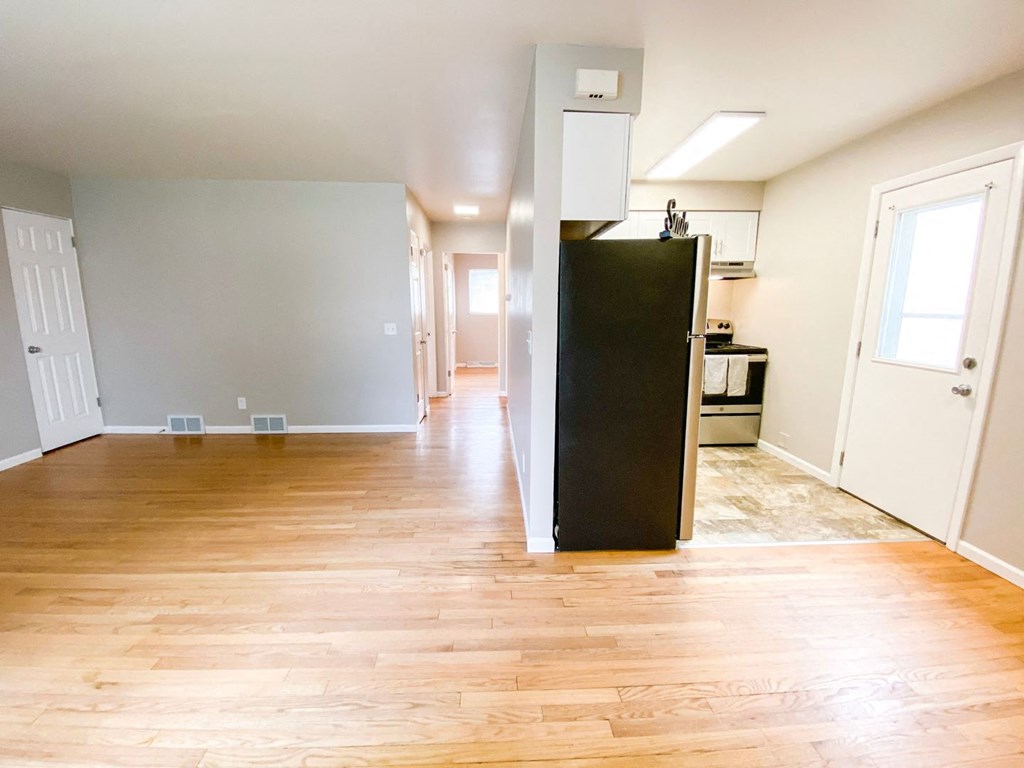 an empty living room and kitchen with wood floors and a refrigerator