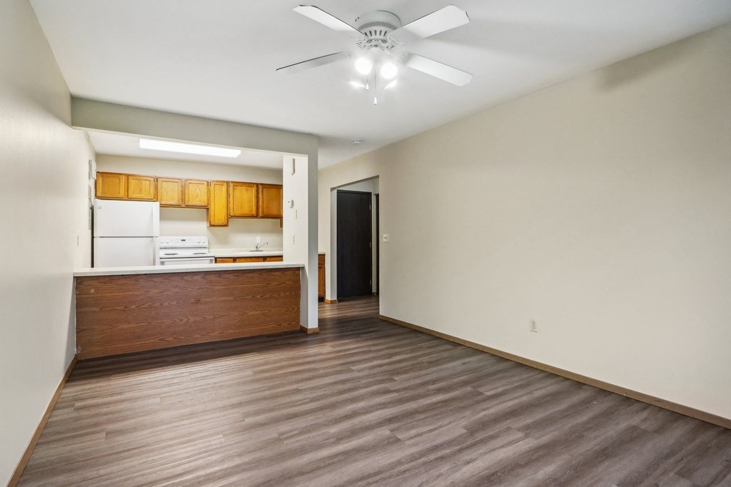 a empty living room with a kitchen and a ceiling fan